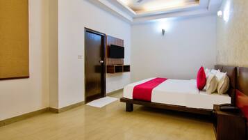 Habitación de hotel con cama, puerta, ventilador de techo y televisor de pantalla plana montado en la pared.