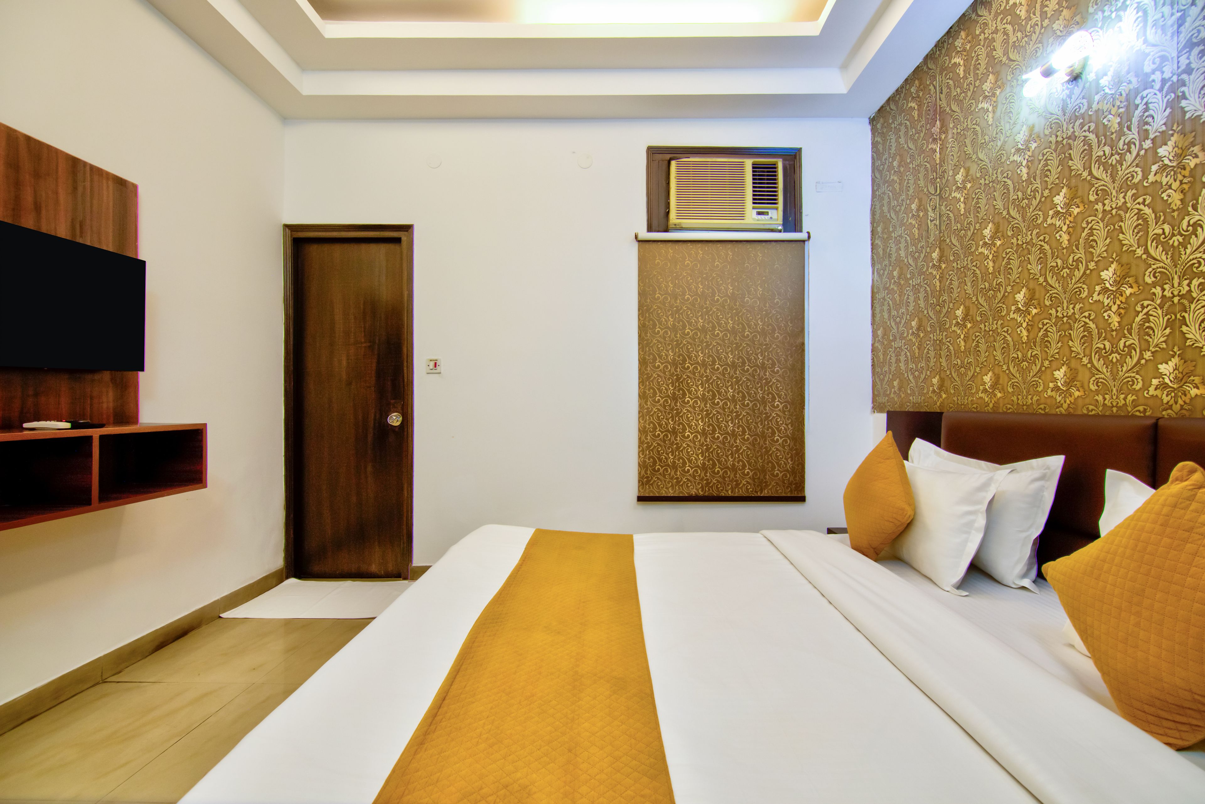 Una habitación de hotel con cama, televisor montado en la pared, puerta y aire acondicionado.