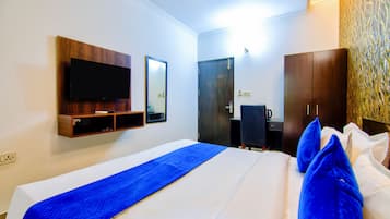 A hotel room with a bed, a television mounted on the wall, a desk with a chair, and a wardrobe.