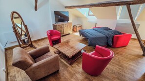 Ein möbliertes Wohnzimmer mit Couch, roten Sesseln, einem Couchtisch aus Holz, einem Fernseher auf einer Holzkommode und einem großen Spiegel.