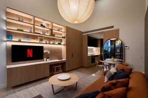 Ein modernes Wohnzimmer mit einem Flachbildfernseher, Holzregalen, einem runden Couchtisch und einer gemütlichen Sitzecke.