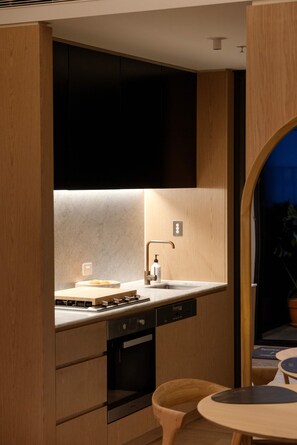 Eine moderne Küche mit Backofen, Spüle und Geschirrspüler. Im Vordergrund steht ein Holzschrank und ein Stuhl.