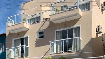 A two-story building with balconies, a car parked in front, and a palm tree.