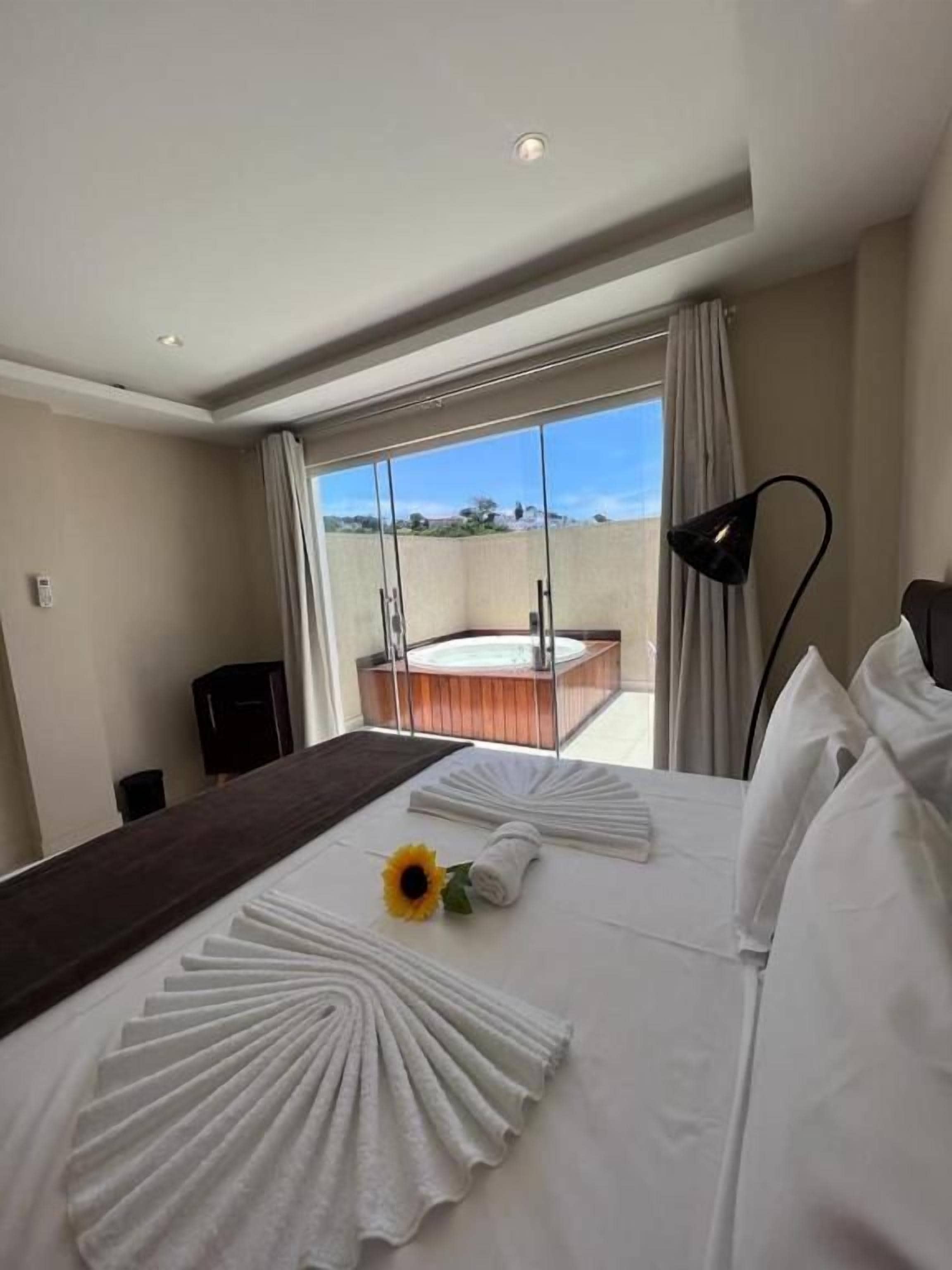 A hotel room with a large bed, a view of the outdoors, a balcony, and a modern lamp.