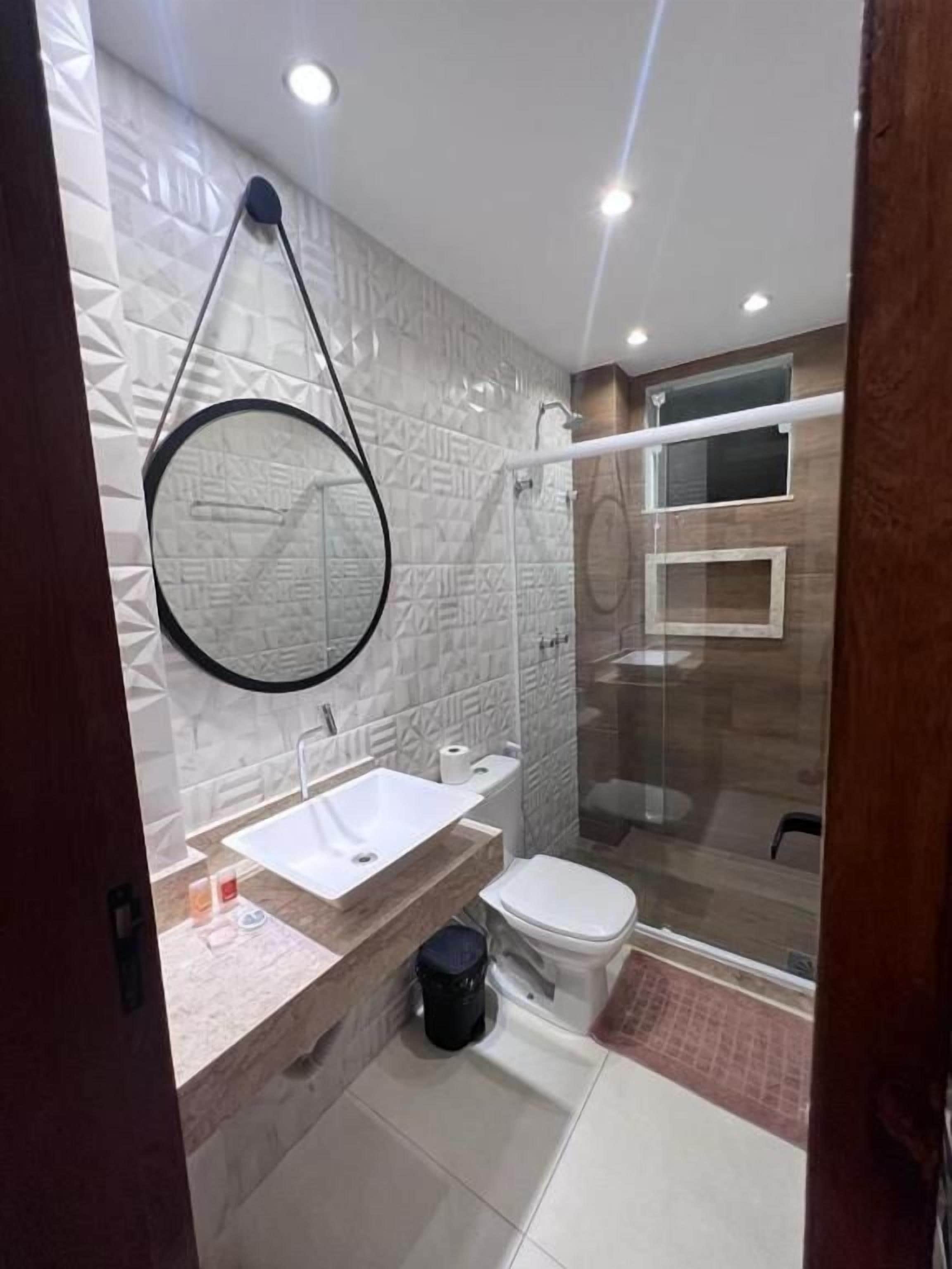 Un baño moderno con lavamanos blanco, inodoro y ducha con mampara de vidrio.