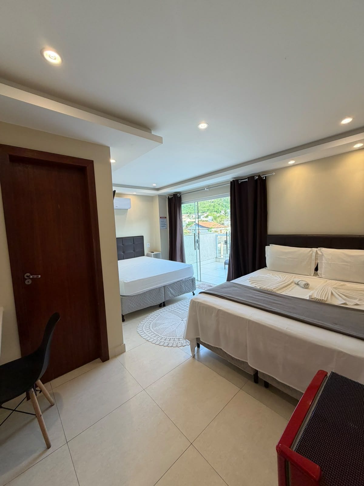 A hotel room with a bed, a desk, and a chair. There is a door and a window with curtains.