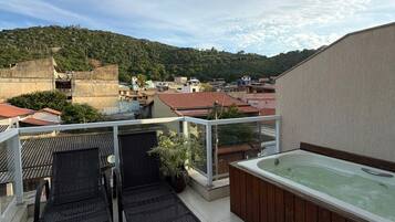 A rooftop terrace with a hot tub, two lounge chairs, and a view of a hillside.
