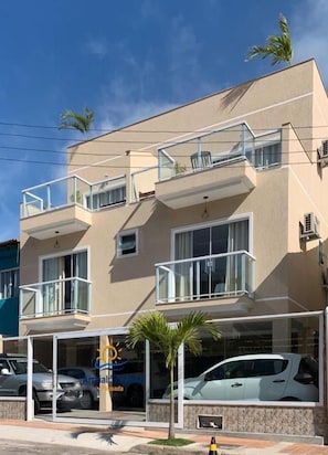 A two-story building with balconies, a car parked in front, and a palm tree. - Pousada Arraial Tropical (Arraial do Cabo)