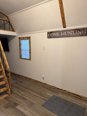 A room with a wooden staircase, a window with blinds, a wall-mounted sign, and a grey rug. - The Marie: Cozy East Texas Stay Near Great Fishing (Quitman)