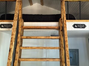 A wooden ladder leading to a room with a black sofa and a door. There are signs on the wall indicating a step. - The Marie: Cozy East Texas Stay Near Great Fishing (Quitman)