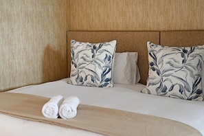 A hotel room with a bed, two pillows with a leaf pattern, and two rolled towels. - Modern Apartment | Secure and Spacious (Cape Town)
