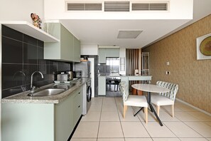 A modern kitchen with a built-in oven, a sink, and a dining area with a table and chairs. - Modern Apartment | Secure and Spacious (Cape Town)