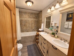 A bathroom with a bathtub, a toilet, a sink, and a shower. There are towels and toiletries on the counter. - Emerald Mountain 28C | Couples Retreat at Mary’s Lake (Estes Park)