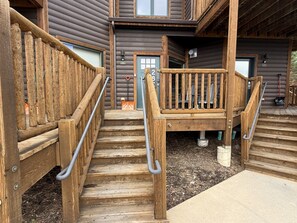 A wooden staircase leading to a building entrance with a metal handrail. - Emerald Mountain 28C | Couples Retreat at Mary’s Lake (Estes Park)