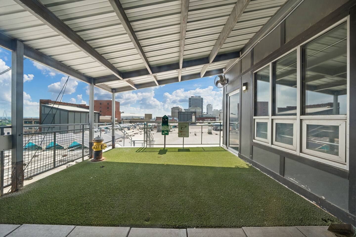 A covered outdoor area with artificial grass, a fire hydrant, and a view of the cityscape.