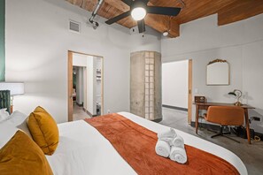 Una habitación de hotel con cama, escritorio, silla, espejo y ventilador de techo.