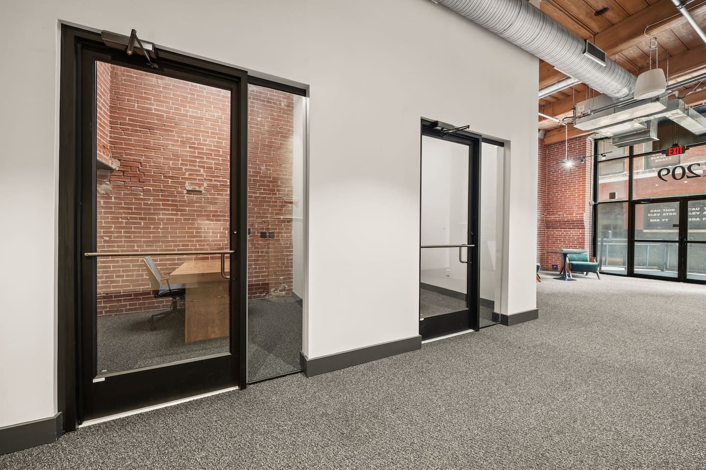 A hallway with glass doors leading to a room with a brick wall, a wooden bench, and a chair.