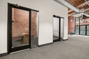 A hallway with glass doors leading to a room with a brick wall, a wooden bench, and a chair.