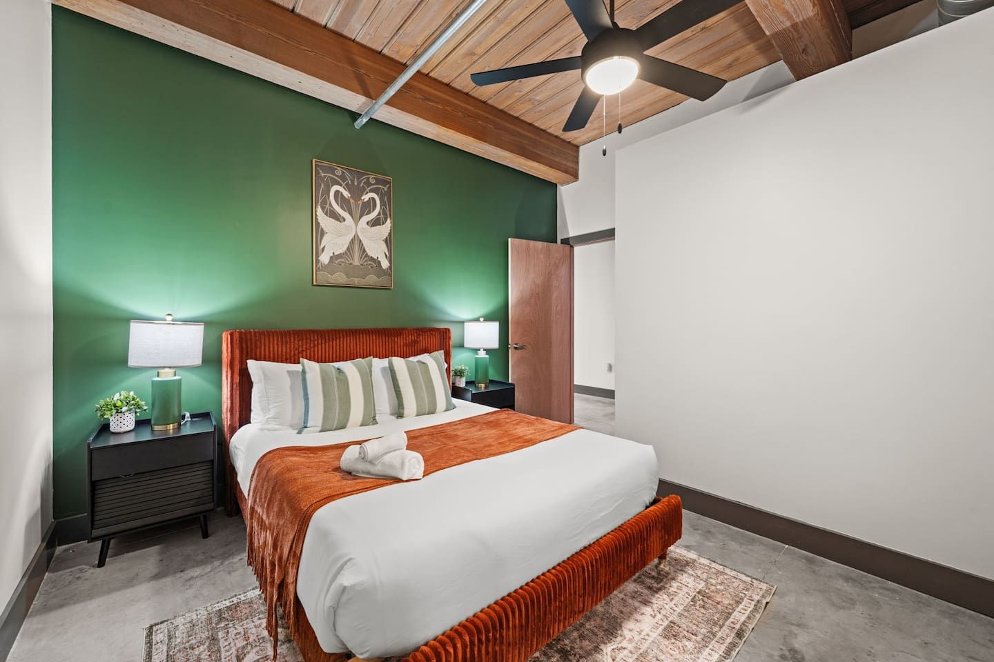 A modern bedroom with a large bed, two bedside tables, a ceiling fan, and a green accent wall.