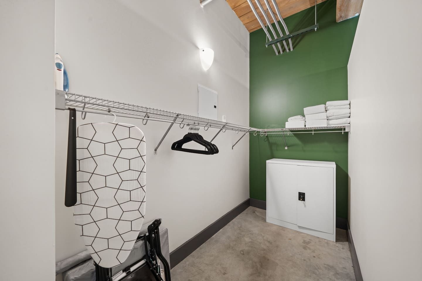 Un espace dédié à la lessive, équipé d’un étendoir, d’une planche à repasser et d’un petit appareil électroménager blanc, probablement un sèche-linge.