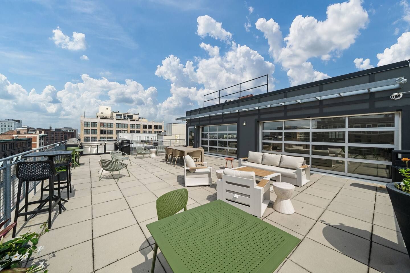 A rooftop terrace with outdoor seating, a grill, and a view of the cityscape.