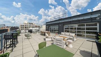A rooftop terrace with outdoor seating, a grill, and a view of the cityscape.