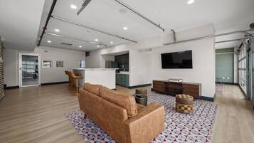 A modern living room with a sofa, ottomans, a TV, and a kitchen in the background.