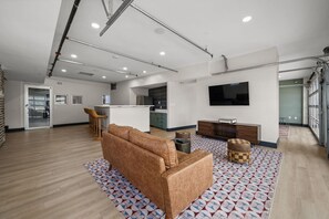 A modern living room with a sofa, ottomans, a TV, and a kitchen in the background. - Walk Busch Stadium | FREE Parking | Gym | RT Patio (St. Louis)