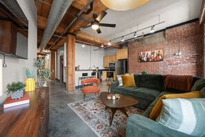 A modern living space with a brick wall, wooden beams, a green sofa, and a dining area.