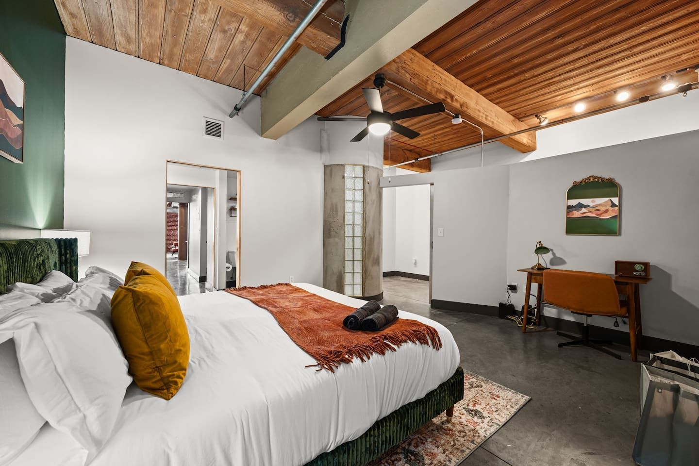 A bedroom with a bed, a desk, and a chair. There is a window and a door.