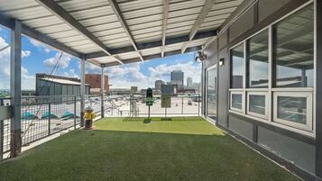 A covered outdoor area with artificial grass, a metal fence, and a view of the cityscape.
