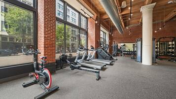 A gym with cardio equipment, weight machines, and a large window overlooking a street.