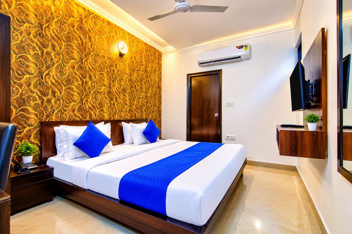 A hotel room with a bed, a ceiling fan, an air conditioning unit, a TV, and a wooden door.