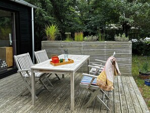 An outdoor wooden deck with a table and chairs, a bench with a towel, and a wooden planter with plants. - Modern holiday home with vaulted ceiling, Tisvilde (Frederiksværk)