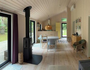 A cozy interior with a central fireplace, a dining area, and a seating space with a view of the outdoors. - Modern holiday home with vaulted ceiling, Tisvilde (Frederiksværk)