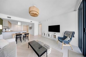 Ein modernes Wohnzimmer mit einer Couch, einem Couchtisch, einem Fernseher und einem Essbereich mit Stühlen und Tisch.