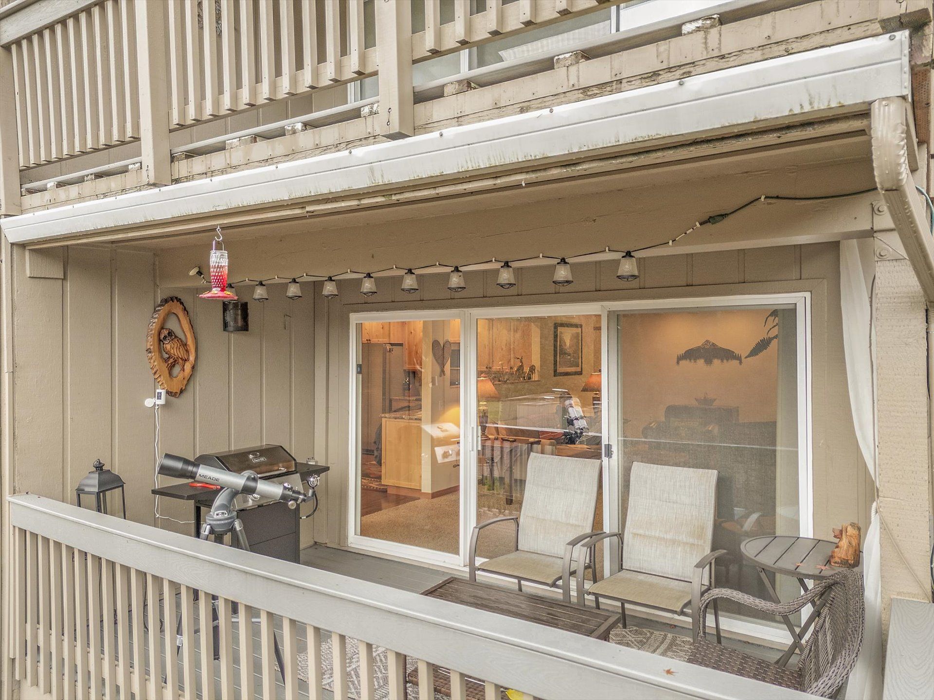 A balcony with a grill, outdoor seating, and a view into the house.