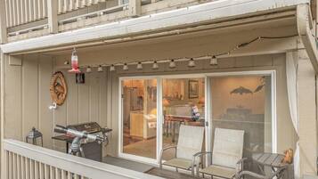 A balcony with a grill, outdoor seating, and a view into the house.