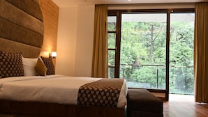 Una camera da letto con un letto grande, una testiera in legno, un comodino con una lampada e vista su una foresta tramite una porta scorrevole in vetro.