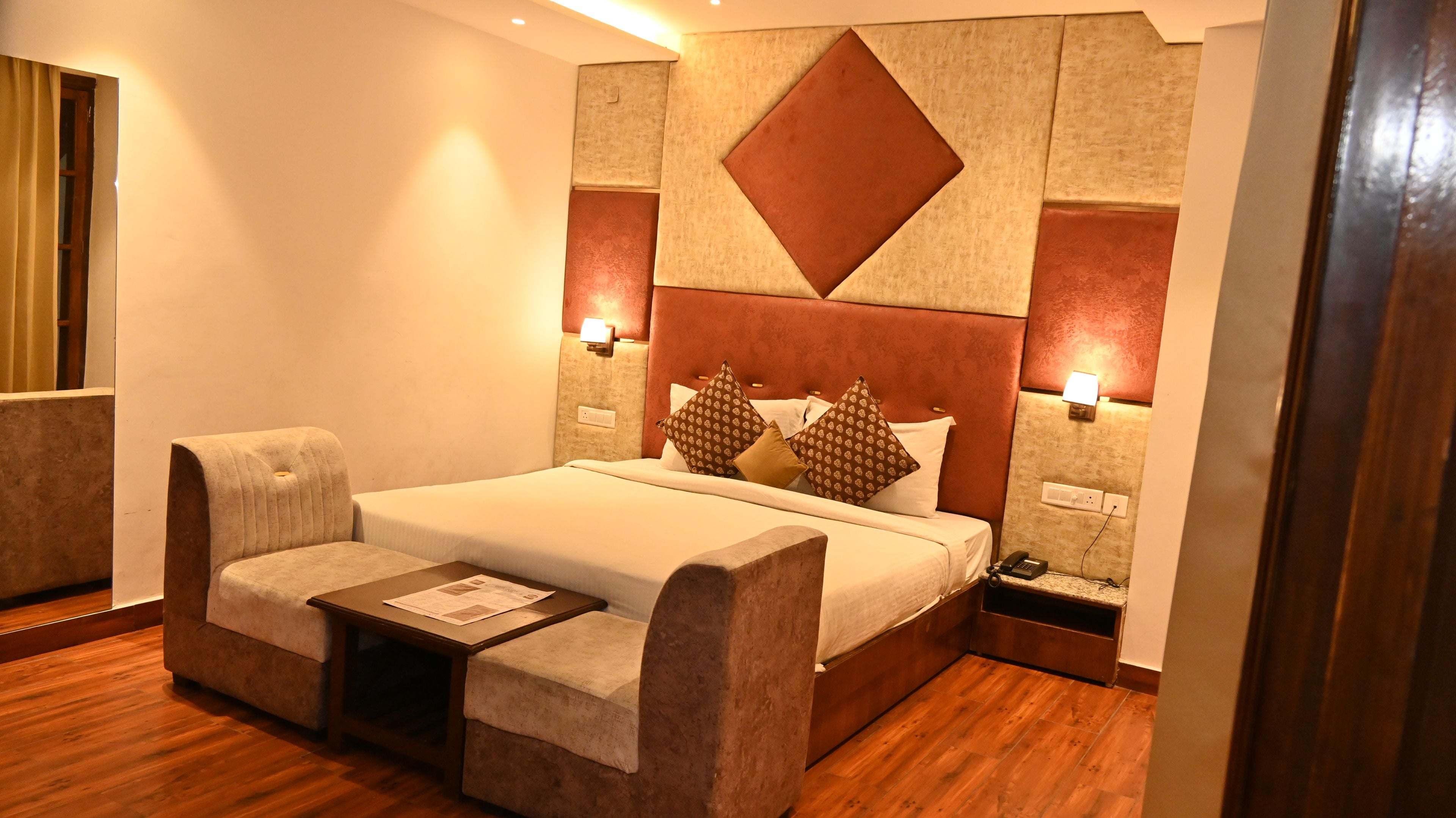 A hotel room with a bed, a sofa, a nightstand, and a wall-mounted phone.