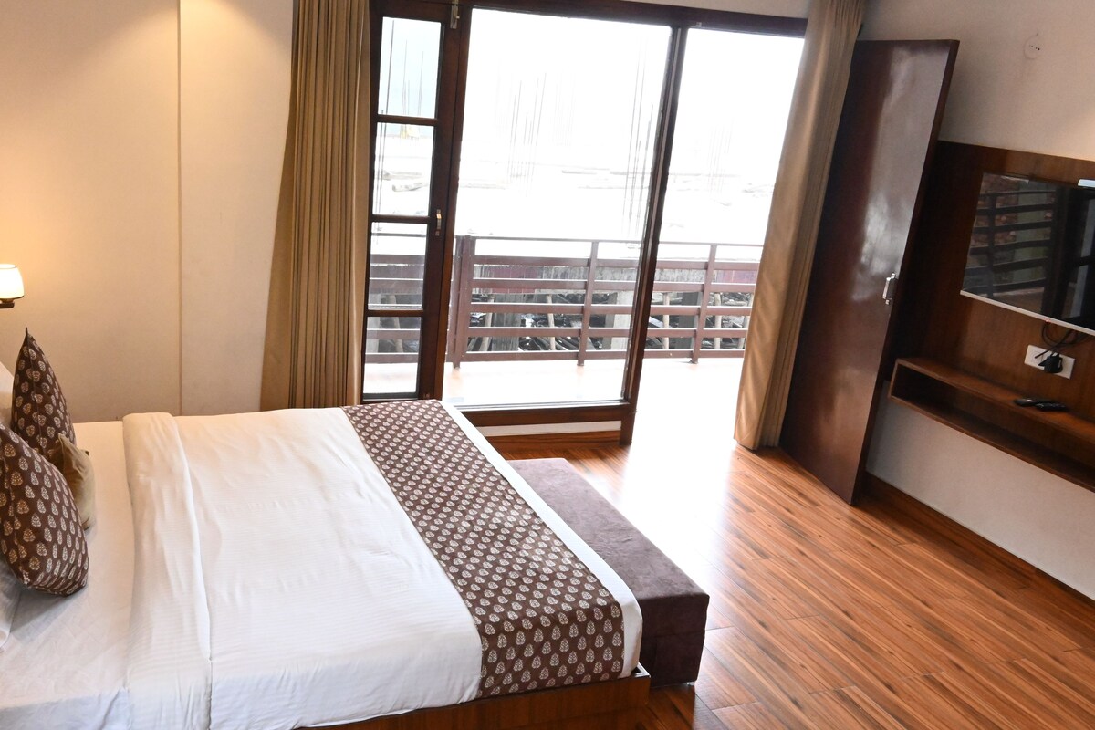 A hotel room with a bed, a television, a wooden floor, and a view of the outside.