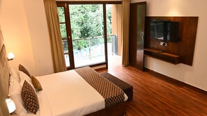 A hotel room with a bed, a TV mounted on the wall, and a balcony with a view of greenery. - Vk Group of hotels  (Dalhousie)