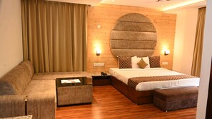 A hotel room with a large bed, a sofa, a coffee table, and a wooden headboard. - Vk Group of hotels  (Dalhousie)