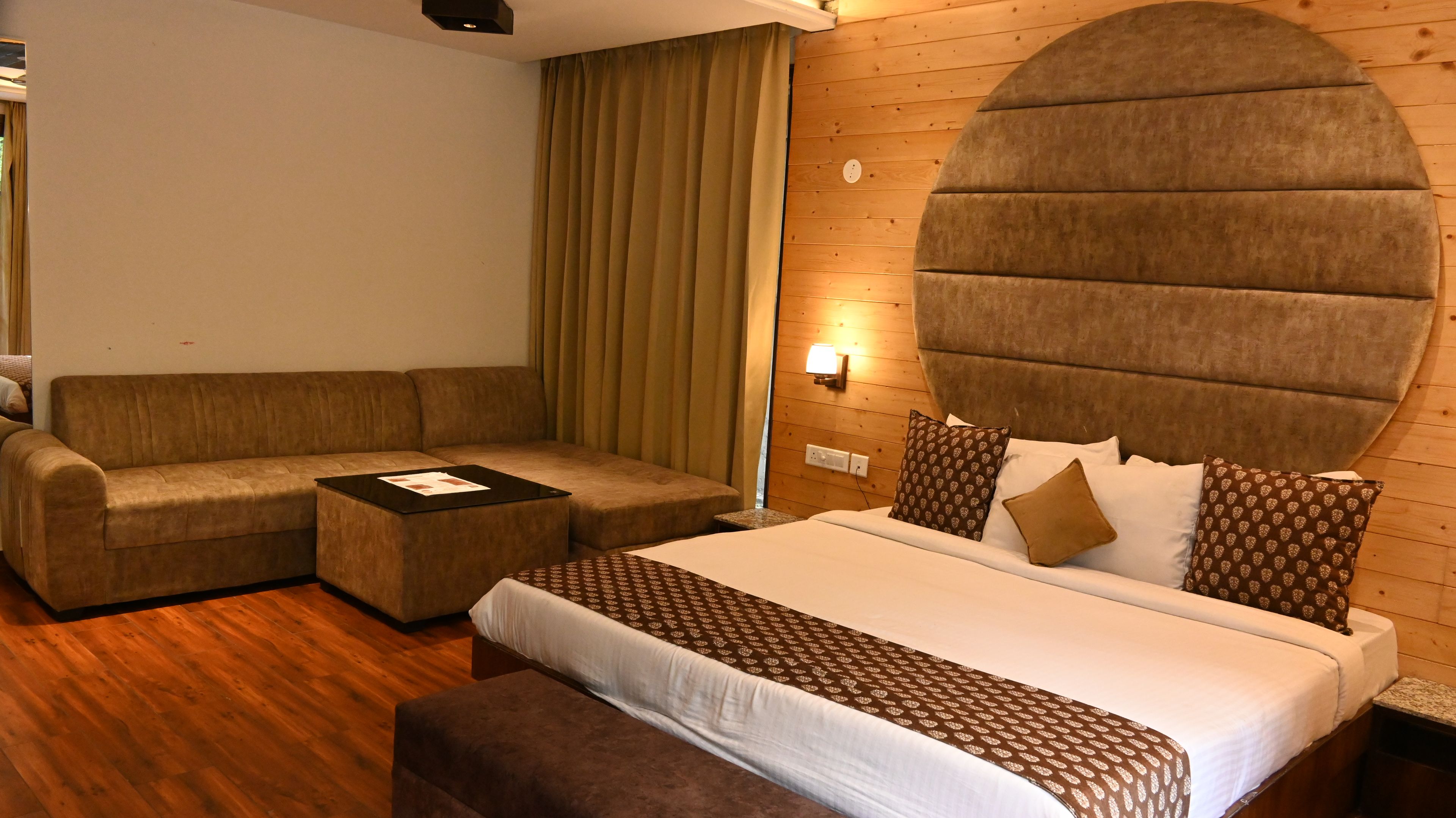 A hotel room with a bed, a sofa, a coffee table, and a wall-mounted light fixture.