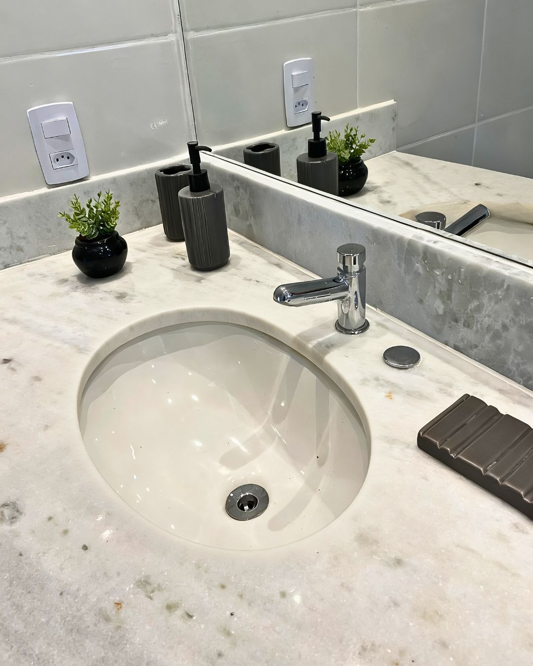 Un baño con lavamanos de mármol, un espejo, un grifo y una pequeña planta en maceta.