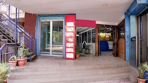 Entrada de hotel con escaleras, un letrero vertical rojo y plantas en macetas.
