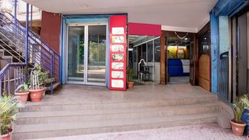 A hotel entrance with a staircase, a red vertical sign, and potted plants.