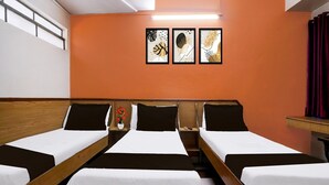 Habitación de hotel con tres camas individuales, una mesita pequeña, una mesita de noche y tres cuadros enmarcados.