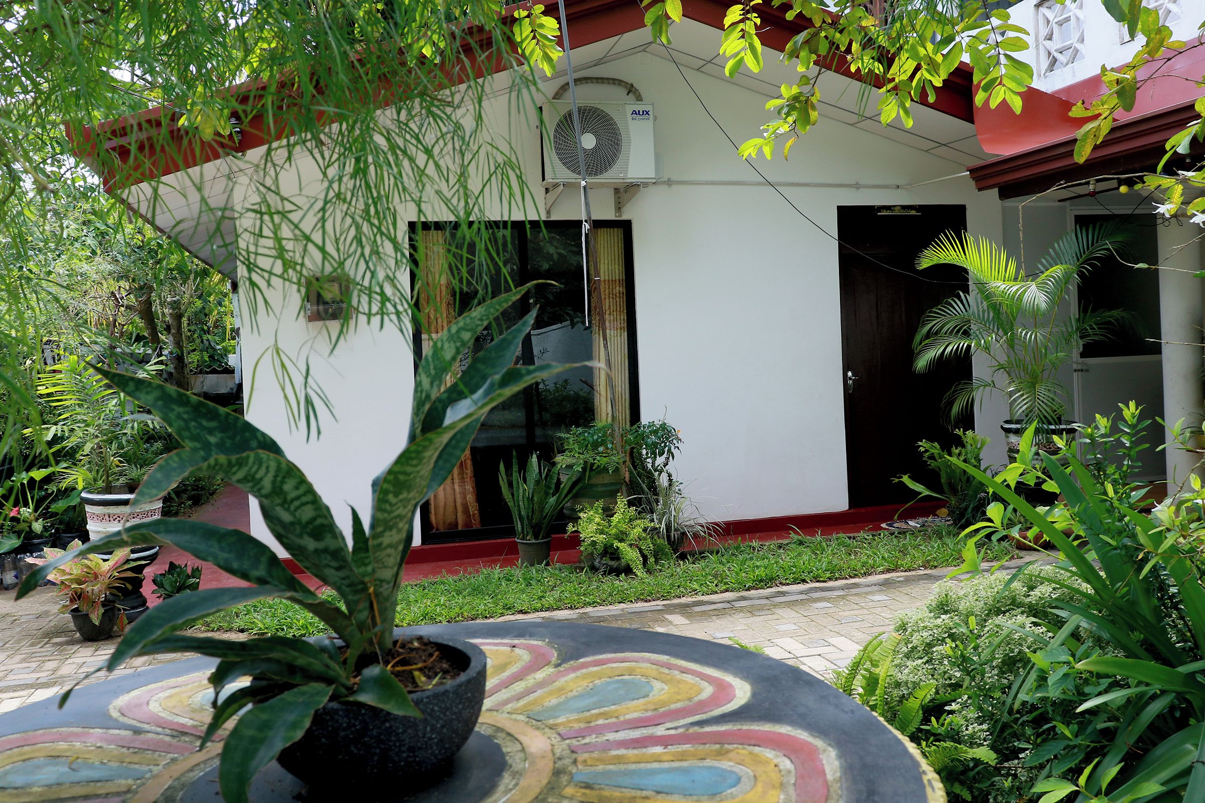 A building with a white exterior, a red roof, and a large window. There is a potted plant in the foreground.