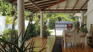 A covered outdoor area with a wooden floor, a table set for dining, and various potted plants. - Nature Beat Villa – Exclusive Tropical Retreat Near Mirissa (kamburugamuwa)